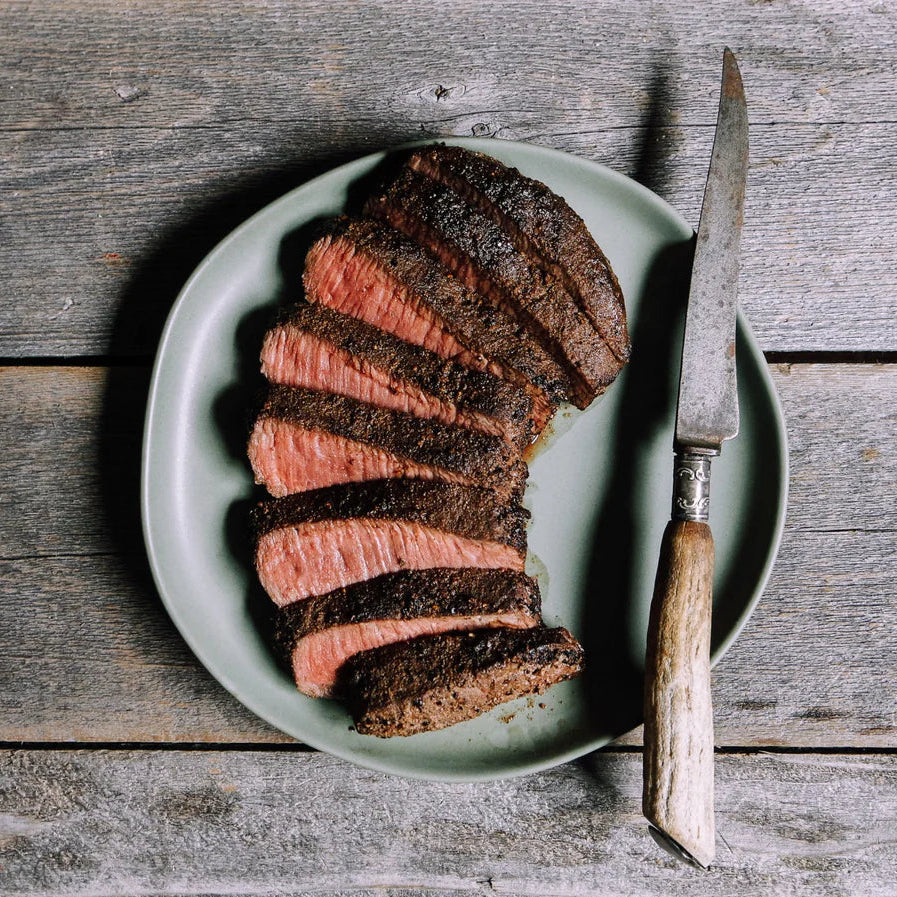 Sliced beef on a green plate with a knife on a wooden surface
