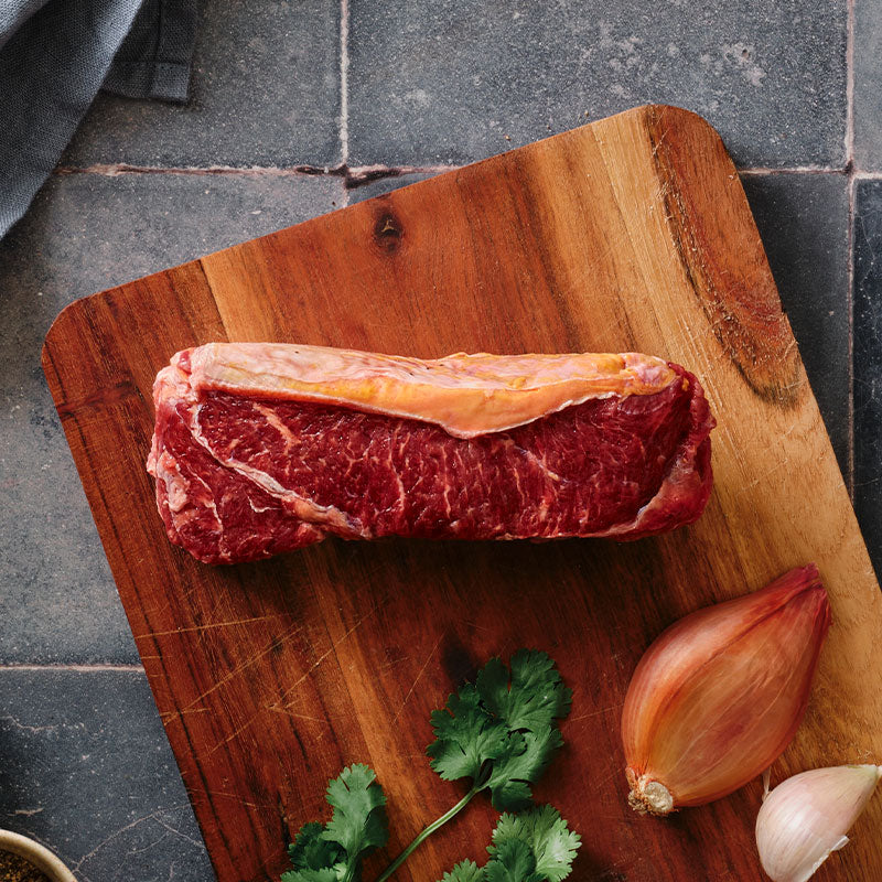 Raw bison steak on a wooden cutting board with an onion and garlic, on a dark stone surface.