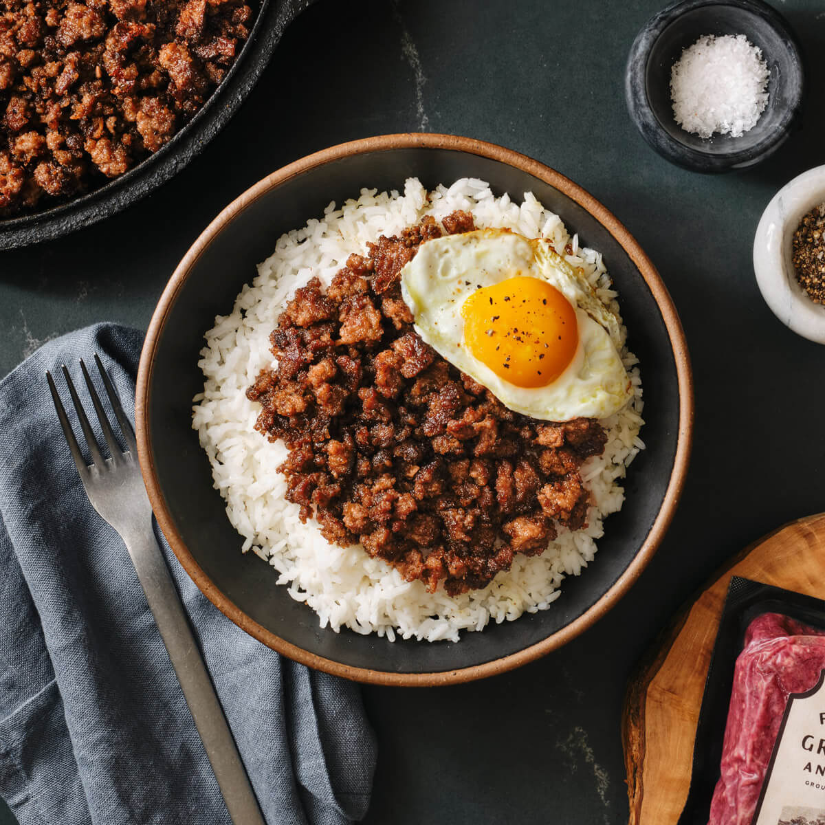Bowl of rice with ground meat and an egg on a dark surface