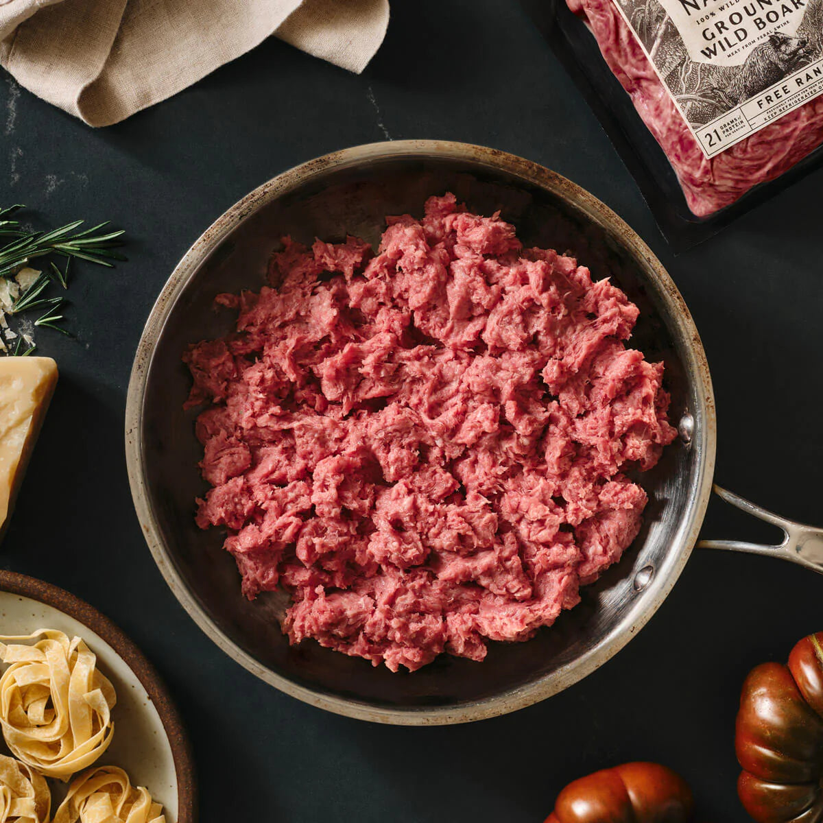 Ground meat in a pan on a dark surface with a package of ground meat in the background.