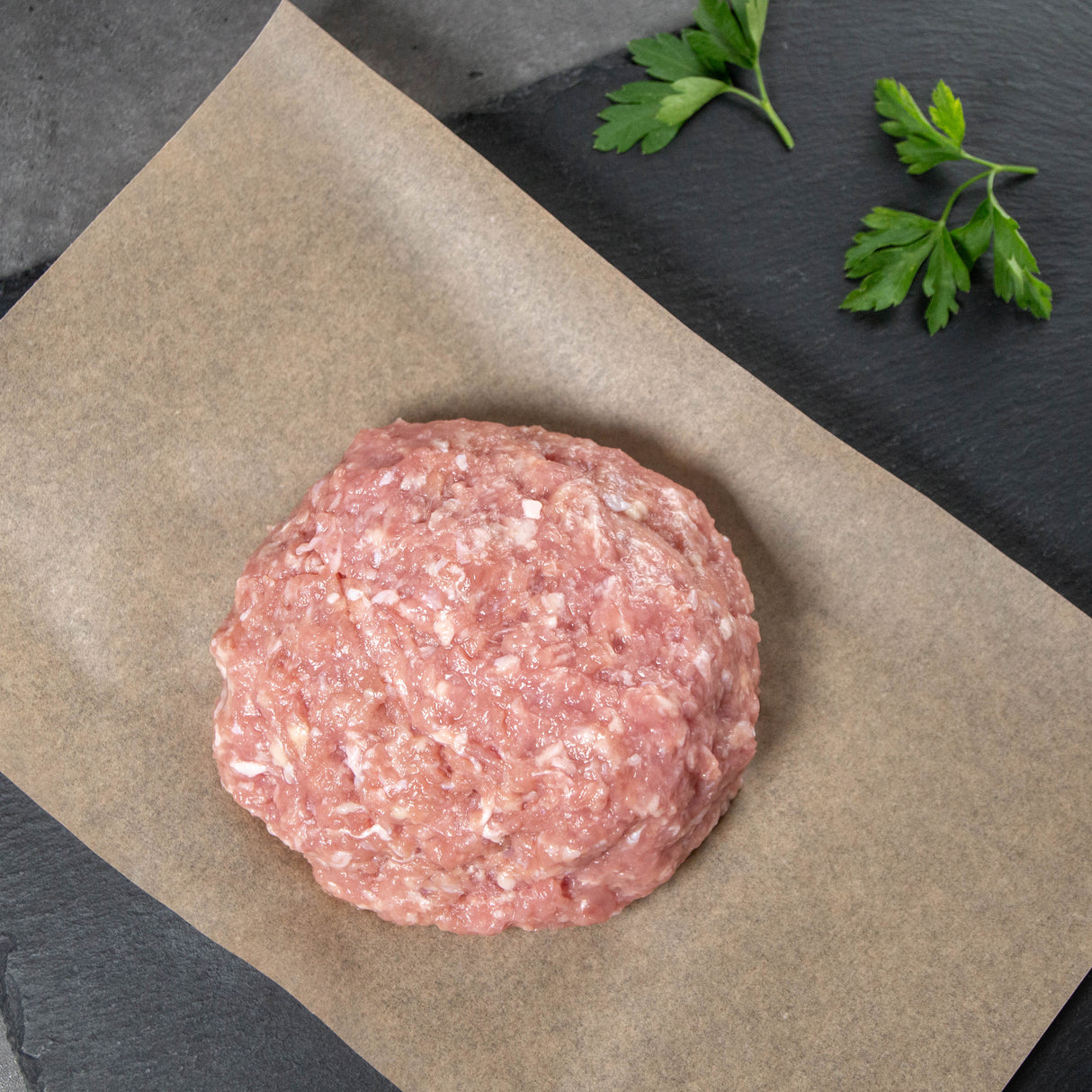 Raw ground turkey patty on brown paper with parsley on a dark surface