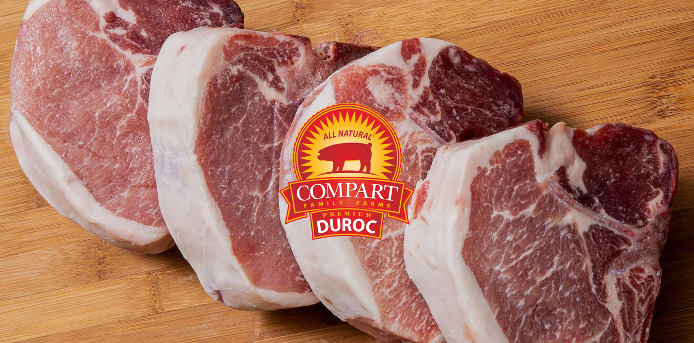 Raw pork chops on a wooden cutting board with Compart Duroc logo.