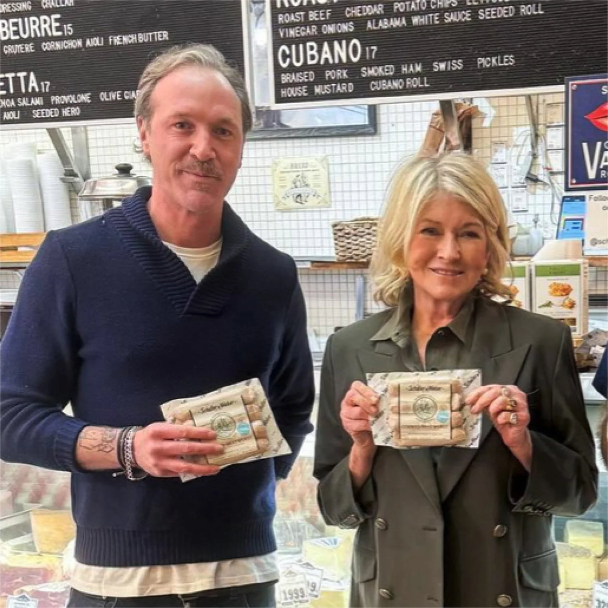 Two people holding packages in a market setting with a menu board in the background.