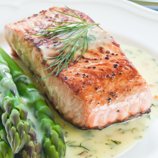 cooked salmon with a dill butter sauce topped with sprig of dill and side of asparagus