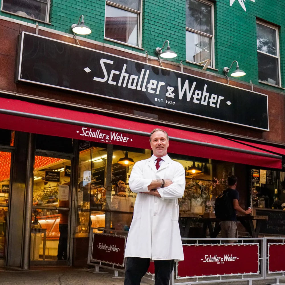 Man in a white coat standing in front of a Schaller & Weber store with a green building facade.