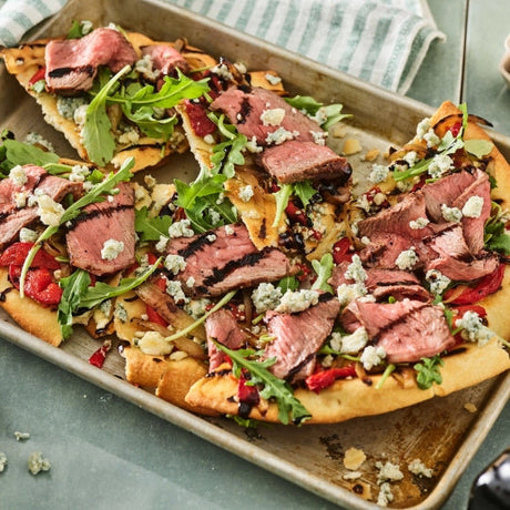 Grilled steak flatbread topped with arugula, caramelized onions, and blue cheese