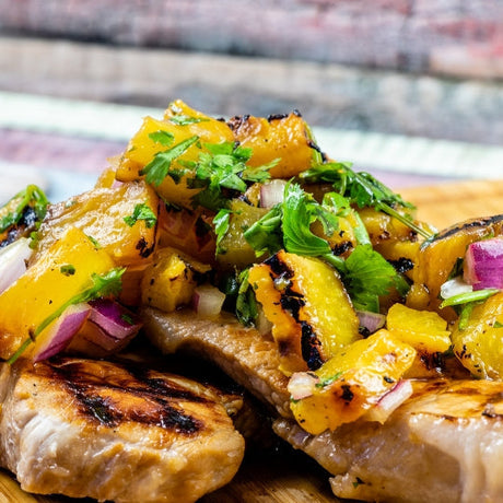 Grilled bone-in pork chops topped with fresh peach salsa on a plate