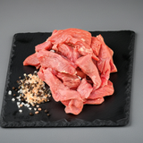 Raw meat slices on a black slate with spices on a gray background