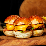 Cheeseburger sliders on a sesame bun on a wooden platter.