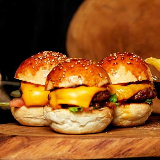 Cheeseburger sliders on a sesame bun on a wooden platter.