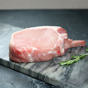 Raw duroc bone-in pork chop on a marble slab with rosemary