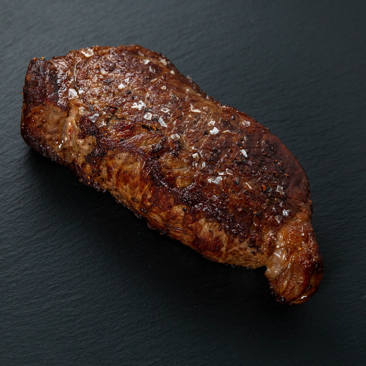 cooked NY strip steak with flake sea salt on top on a slate cutting board.
