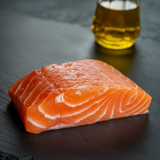 Raw faroe island salmon fillet on a dark slate surface with a small glass of oil.