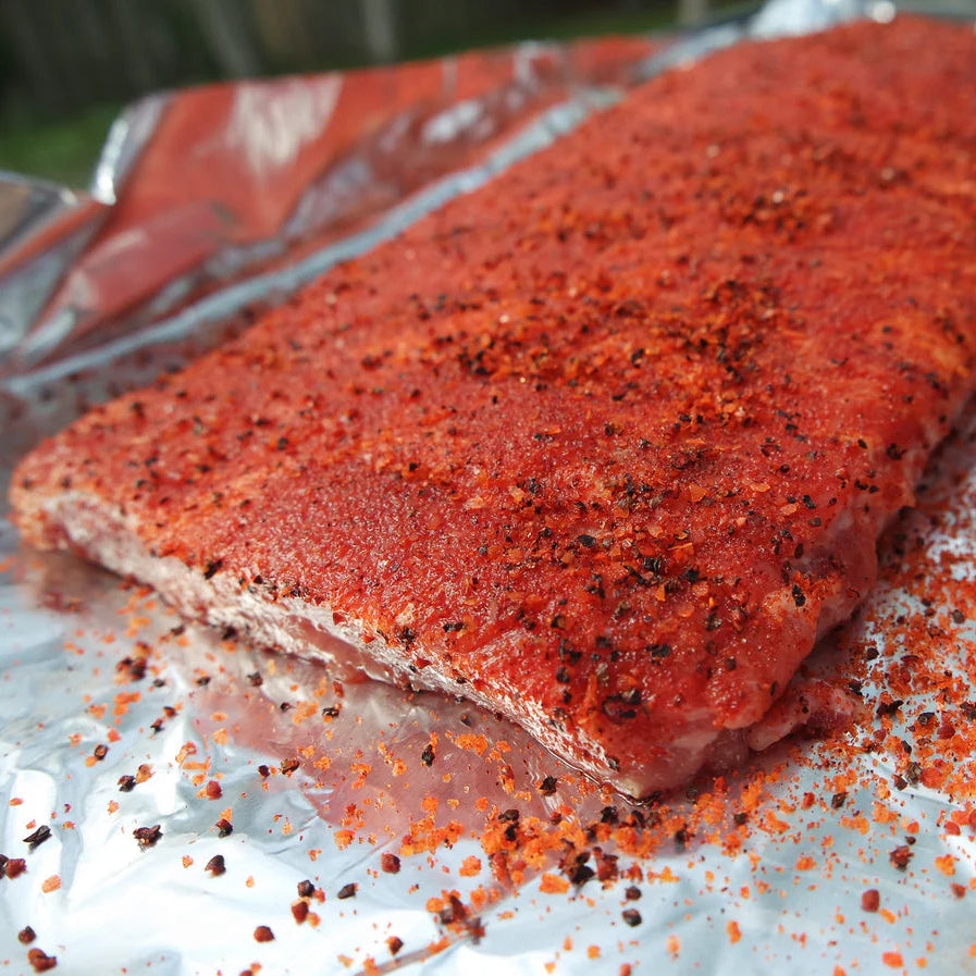 Two pieces of seasoned raw meat on a sheet of tinfoil.