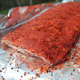 Two pieces of seasoned raw meat on a sheet of tinfoil.