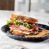 Sandwich with ham, cheese, lettuce, and tomato on a blue plate with a blurred background