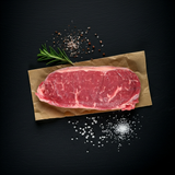 Thousand Hills Grass-Fed Strip Steak on butcher paper with rosemary and sea salt, photographed on a dark slate background in warm natural light.